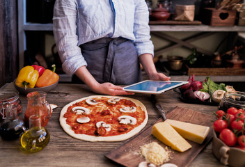 Fresh pizza with tomato and mushrooms. Homemade tasty pizza on dark wooden background. Raw dough for pizza with ingredients and spices on wooden rustic table. Traditional Italian food. Soft focus.