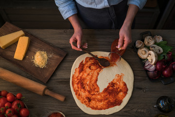 Fresh original Italian raw pizza and ingredients on wooden table, preparation in traditional style. Woman cooking homemade pizza on a wooden table in a home kitchen. Cooking, food and people concept.