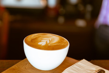 Hot latte coffee art drink, white cup on dark wood in coffee shop.