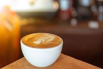 Hot latte coffee art drink, white cup on dark wood in coffee shop.