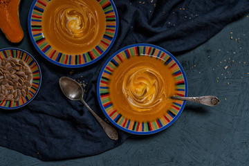 Seasonal autumn food. Spicy pumpkin ans carrot soup with cream and seasoning in rustic bowl on dark gray background. Hot, fresh vegetable soup. View from above with copy space. Toned image.
