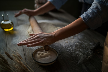 Homemade raw dough on a rustic wooden table. Making pizza. Dough with a rolling pin. Flour, butter, wheat spikelets. Concept of cooking and food. Toned image.