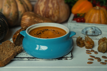 Pumpkin soup in a bowl with autumn vegetables and pumpkin seeds. Vegan soup. Vegetables cream soup and ingredients. Concept of healthy eating or vegetarian food. Toned image. Selective focus.
