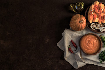 Pumpkin soup in a bowl with autumn vegetables and pumpkin seeds. Vegan soup. Vegetables cream soup and ingredients. Concept of healthy eating or vegetarian food. Top view with copy space. Toned image.