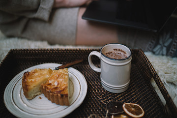 The girl sitting on a wooden floor. Laptop and coffee cup. Feet in woollen socks. The woman relaxes in cozy home. Winter and Christmas holidays concept. Selective focus. Toned image.