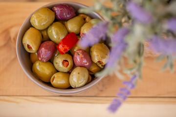 Olives stuffed with red pepper and herbs spices. Multi-colored olives in a small bowl on a wooden table. Lavender. Blurry background. Closeup. Soft focus. Copy space. Top view.