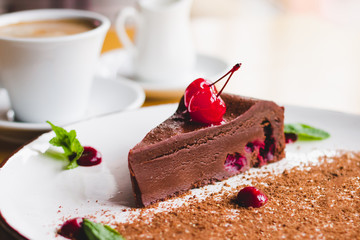 A cup of coffee with a chocolate brownie cake with cherries and mint. Sweet сhocolate dessert in a cafe. Homemade sweets recipes