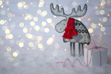 Small gift box with vintage wooden deer against a background bokeh of twinkling lights. Luxury New Year gift. Christmas background with gift box. Christmastime celebration. Copy space for you text.