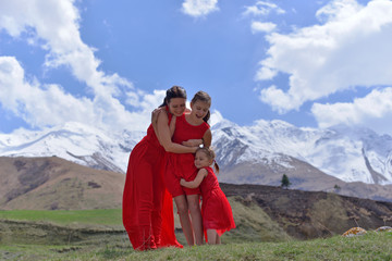 Fototapeta na wymiar A young woman with two daughters in red dresses resting in the snow-capped mountains in the warm spring.