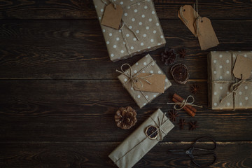Christmas background with decorations and craft paper gift boxes on rustic wooden board. Presents, decoration, fir cones, anise stars and twine ribbon. Preparation for the happy holidays. Toned image.