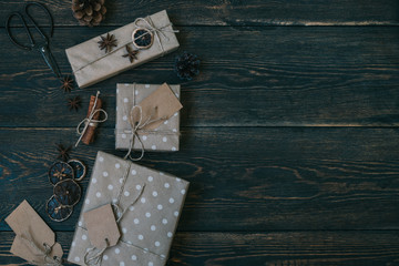 Christmas background with decorations and craft paper gift boxes on rustic wooden board. Presents, decoration, fir cones, anise stars and twine ribbon. Preparation for the happy holidays. Toned image.