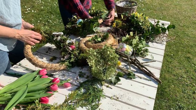 Mother and daughter tie easter wreaths, spring wreaths, summer wreaths outdoors in sunshine and are happy