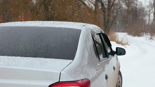 Car vehicle in snowfall. Winter snowy weather.  Fluffy snowflakes fall smoothly on the windshield and car body slow motion
