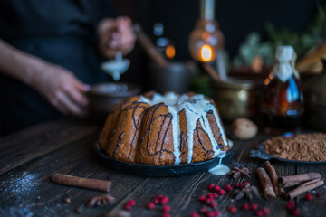 Holiday cake on wooden table with berry, spice and chocolate at rustic home kitchen. Christmas baking background. Ingredients for cooking on dark wooden background. Homemade festive food. Toned image