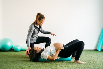 Pregnant woman doing fitness ball and pilates exercise with coach. Happy future mother preparing for childbirth. - obrazy, fototapety, plakaty