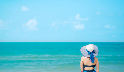 Fototapeta na wymiar Woman enjoying beach relaxing joyful in summer by tropical blue water. Bikini model on travel wearing beach hat.