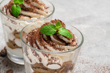 two portions Classic tiramisu dessert in a glass on concrete background