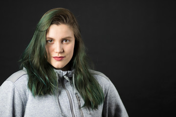 Beautiful brunette girl with dyed green hair on black background.