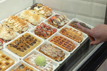 A woman chooses at popular street food, Belgium waffle and traditional dessert.