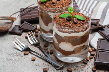 two portions Classic tiramisu dessert in a glass and chocolate bar on concrete background