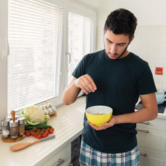 Young handsome man is having breakfast in the kitchen at home. The guy prepared himself oatmeal and a glass of milk for breakfast.