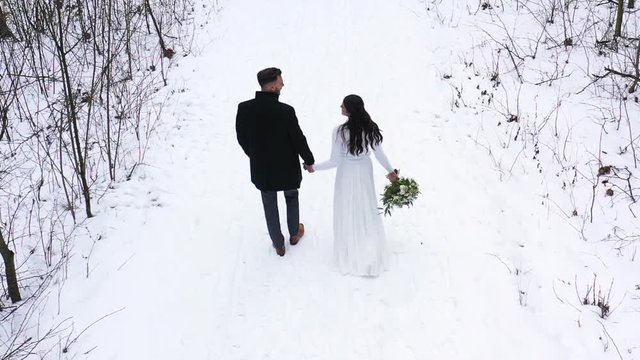 View of striding newlyweds bride and groom holding wedding bouquet from aerial view.