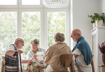 Group of senior friends sitting together at the table at nursing home dining room