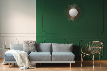 Golden sun shape like mirror on green wall of living room interior with scandinavian sofa with...