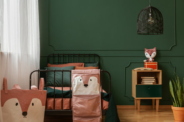 Real photo of black, metal bed standing against dark green wall with molding in a teenager's bedroom interior with fox decorations