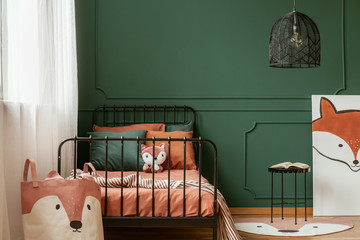 Fox-themed kid bedroom interior with molding on green wall and orange sheets on the bed. Real photo