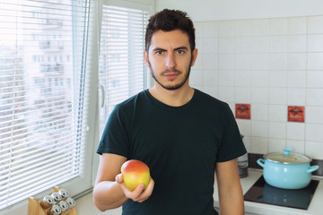 A young man is holding a ripe organic apple. He proposes to join a healthy lifestyle.