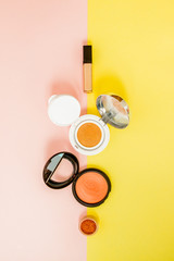 Make up products spilling on to a bright yellow and pink background with copy space