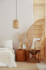 White and bright bedroom interior with wicker peacock chair with white pillow, rattan lamp and...