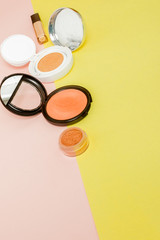 Make up products spilling on to a bright yellow and pink background with copy space