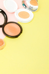 Make up products spilling on to a bright yellow and pink background with copy space