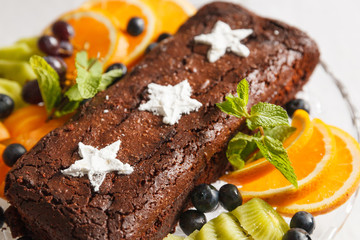 Chocolate brownie cake with fresh blueberries, white stars made of powdered sugar, orange slices, kiwi and mint leaves. Homemade cake decorated with fruit. Festive concept