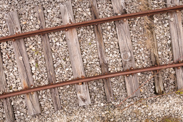 Old rusty rails on cracked wooden sleepers sprinkled with small stones. Top view of the vintage railway tracks. Closeup of part of the way
