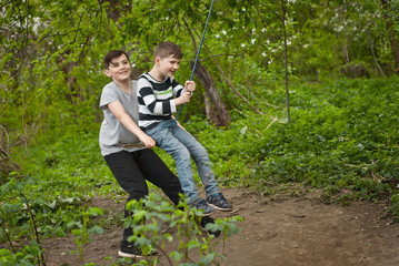Children are riding a swing in the park. Guys on a homemade swing from ropes and boards.