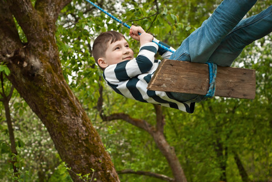 Children are riding a swing in the park. Guys on a homemade swing from ropes and boards. Light blur as an artistic effect of motion.