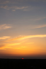 Fototapeta premium the pink sun sets over the city skyline, illuminating the orange clouds