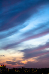 blue-pink sunset sky with dramatic clouds against the bokeh lights of the city
