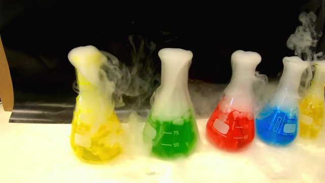 Colorful solutions in a chemistry laboratory boiling while white smoke coming out of the conical in pan motion