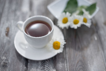 Obraz na płótnie Canvas Tea in a white cup on a wooden table. Daisies on the table