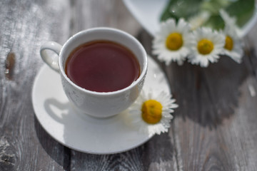 Tea in a white cup on a wooden table. Daisies on the table