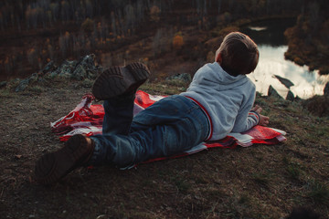 The child lies on a red blanket in the mountains and looks at the sky