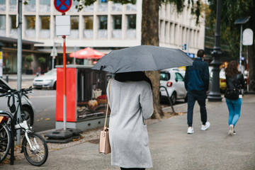 A woman with an umbrella is walking along the street of Berlin in Germany in rainy weather.