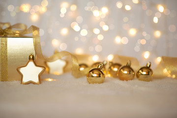Gold Christmas background of defocused twinkling lights with gold balls, decoration and gift box. Selecnive focus. Toned image with copy space for your text.