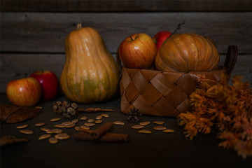 Spice, fall leaves and cones on warm dark wooden table. Defocused colorful vegetables on the background. Organic vegetables in a wicker basket. Eco food and harvest concept. Selective focus.