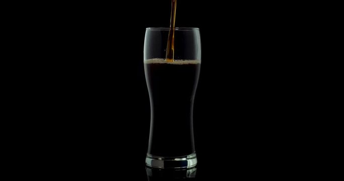 beer with foam is poured into a glass against a dark background. 4k