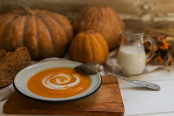 Homemade autumn butternut squash soup with bread. Roasted pumpkin and carrot soup with cream and pumpkin seeds on white wooden background. Concept of healthy eating food. Toned image.